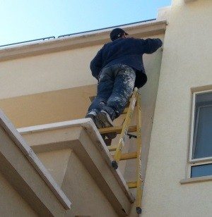 man painting a house on a stepladder